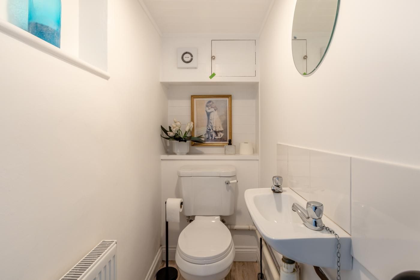 A compact bathroom with a toilet, sink, and a framed artwork above the toilet.