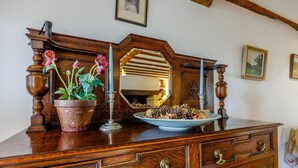 Een houten dressoir met een spiegel, een potplant en een decoratief bord met dennenaalden.