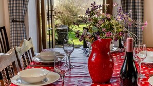 Uma mesa de jantar posta com pratos, tigelas e copos de vinho brancos, um vaso vermelho com flores e uma garrafa de vinho.