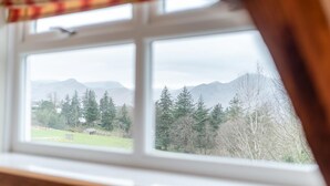 Ein Fenster mit Blick auf eine gebirgige Landschaft, Bäume und ein Gebäude in der Ferne.