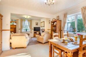 A spacious living room with a sofa, chairs, a dining table with breakfast, and a TV.