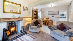 A cozy living room with a fireplace, two armchairs, a dining table, and a kitchen area visible through an open door. - 2 Bed in Welney (oc-o30872) (Welney)