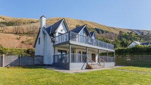 A two-story house with a balcony, a chimney, and a view of a hill.