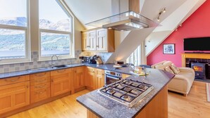 A modern kitchen with wooden cabinets, a gas stove, and a large window overlooking a mountainous landscape.