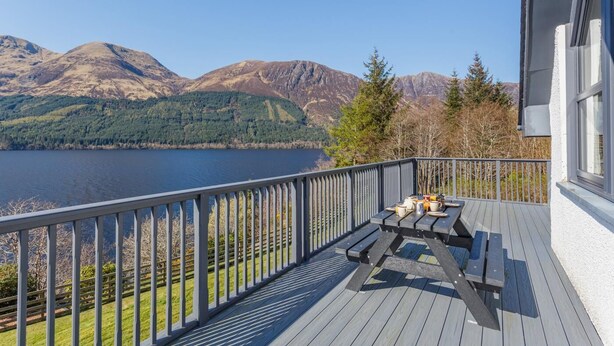 A deck with a table and chairs overlooking a lake and mountains.