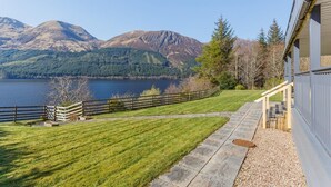 A lakeside property with a stone pathway leading to a wooden deck, overlooking a lake and mountains.