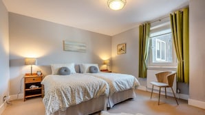 Une chambre avec deux lits, des lampes de chevet, une chaise, une fenêtre avec des rideaux et un radiateur.