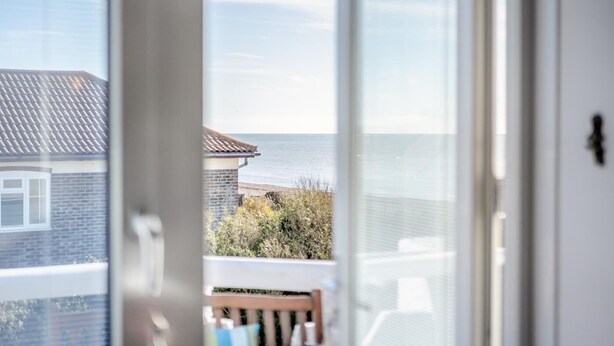 Une vue depuis un balcon, avec un ciel dégagé et un bâtiment éloigné doté d’un toit en tuiles.