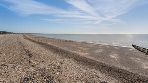 Une plage de galets bordée d’une clôture en bois, sous un ciel dégagé.
