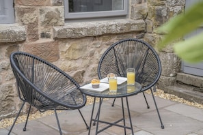Zwei schwarze Korbstühle um einen kleinen Tisch mit einem Muffin und zwei Gläsern Orangensaft.