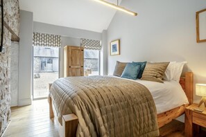 Ein Schlafzimmer mit Bett, Holz-Kopfteil, Nachttisch und Blick ins Freie.