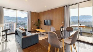 A modern living room with a sofa, dining table, chairs, a TV, and a balcony with a city view. - |EP| Nice Apt w/View, Balcony & Gym in El Poblado (Medellín)