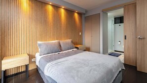 A modern bedroom with a large bed, wooden panel wall, bedside tables, and a walk-in closet. - |EP| Nice Apt w/View, Balcony & Gym in El Poblado (Medellín)