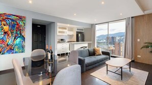 A modern living room with a glass table, grey sofa, and a city view through large windows. - |EP| Nice Apt w/View, Balcony & Gym in El Poblado (Medellín)