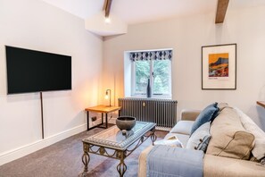 A living room with a flat-screen TV, a table with a bowl, a radiator, a window with curtains, a sofa, and a framed picture on the wall.