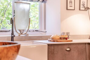 A kitchen with a large window, a sink, a countertop with bread and a cutting board, and a wall-mounted light fixture. - 1 Bed in Nant-y-derry (oc-g30807) (Nant-y-derry)