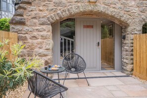 An outdoor seating area with stone walls, a door with a sign, and a small table with chairs.