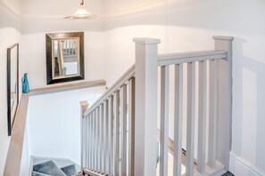 A staircase with white railings, a wooden handrail, and a light fixture above.