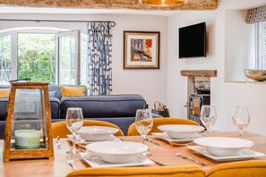 A dining area with a table set for four, a sofa, a fireplace, and a TV mounted on the wall. - 2 Bed in Nant-y-derry (oc-c30806) (Nant-y-derry)