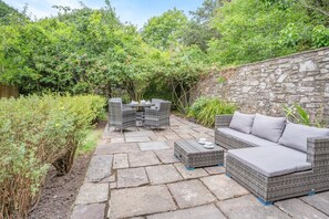 An outdoor patio with stone flooring, wicker furniture, and a stone wall. - 2 Bed in Nant-y-derry (oc-c30806) (Nant-y-derry)