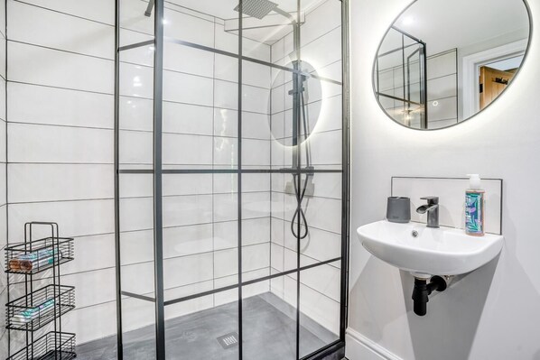 A modern bathroom with a glass-enclosed shower, a white sink, and a round mirror.