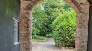 Un arco de piedra que da paso a un camino rodeado de vegetación.