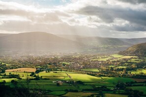 A panoramic view of a valley with a town, green fields, and distant hills.
