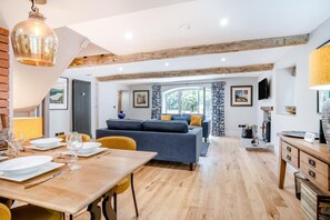 Una sala de estar moderna con comedor, vigas de madera, un sofá y un televisor.