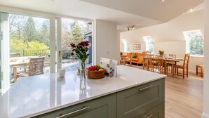 Une cuisine moderne dotée d’un grand îlot central, d’une table à manger en bois et de chaises, et qui est attenante à un espace de vie comprenant un canapé et une table à manger.