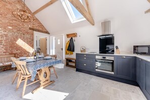 Une cuisine moderne dotée d’une verrière, d’une table à manger en bois et d’appareils électroménagers intégrés.