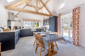 A modern kitchen with dark cabinets, a dining area with a patterned tablecloth, and a view through the glass door. - 2 Bed in Moulton St. Mary (oc-c30849) (Moulton Saint Mary)