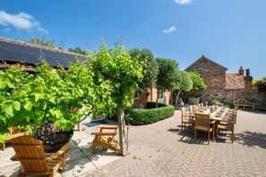 An outdoor dining area with brick flooring, wooden tables and chairs, and a pergola with green vines. - 6 Bed in Walsingham (oc-r30797) (Little Walsingham)