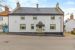 A two-story white building with a green door, multiple windows, and a small porch with potted plants. - 6 Bed in Walsingham (oc-r30797) (Little Walsingham)