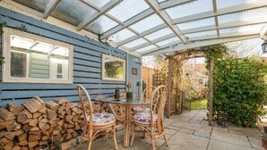 A covered patio with a table and chairs, a stack of firewood, and a glass enclosure. - 2 Bed in Wimborne (oc-s30924) (Wimborne)