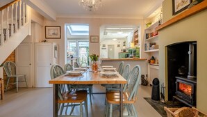 A dining area with a wooden table set for six, surrounded by light blue chairs. A chandelier hangs from the ceiling, and a fireplace is visible to the right. - 2 Bed in Wimborne (oc-s30924) (Wimborne)