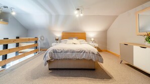 Un dormitorio con cama, mesitas de noche, cómoda, ventilador y baranda de madera.