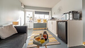 Un espacio habitable compacto con un sofá, una mesa de centro con provisiones para el desayuno, una cocina equipada y vistas a través de un ventanal.