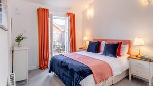 Quarto com cama, duas mesas de cabeceira, um criado-mudo, janela com cortinas e vista para o exterior.