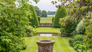 Ein gepflegter Garten mit einem zentralen Brunnen, ordentlich geschnittenen Hecken und einem ruhigen Teich.