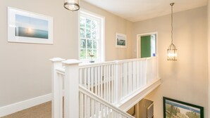 Eine Treppe mit weißen Geländern führt zu einer oberen Etage, ein großes Fenster bietet Blick auf Grünflächen, und ein gerahmtes Bild hängt an der Wand.