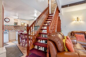 Eine Treppe führt zu einem Schlafzimmer im oberen Bereich, einem Essbereich mit einer Küche im Hintergrund und einem Ledersofa mit Kissen.