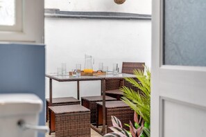 Ein Korbtisch mit Stühlen, eine Karaffe und Gläser auf einem Balkon.
