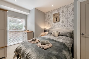 Ein Schlafzimmer mit Bett, Nachttisch, Lampe, einem Fenster mit Jalousien und einer Wand mit dekorativem Muster.