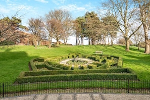 Ein gepflegter Garten mit einem kreisförmigen Heckenlabyrinth, einer Bank und verschiedenen Bäumen.