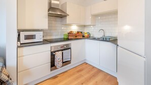 Une cuisine moderne avec des armoires blanches, une hotte de cuisinière en acier inoxydable, un four à micro-ondes, un four encastré et un évier.