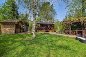 A wooden cabin with a patio, a barbecue area, and a pergola with vines.