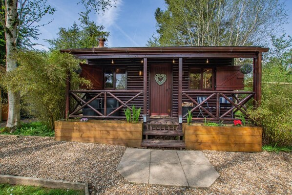 A wooden cabin with a porch, a heart-shaped decoration, and a gravel driveway.