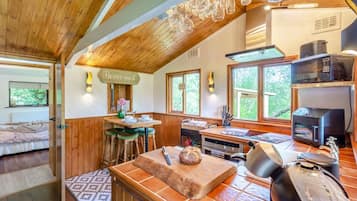 A cozy kitchen with wooden beams, a dining area with stools, and a view of greenery outside.