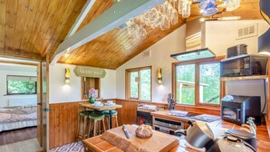 A cozy kitchen with wooden beams, a dining area with stools, and a view of greenery outside.