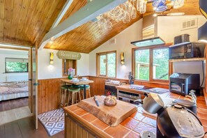 A cozy kitchen with wooden beams, a dining area with stools, and a view of greenery outside.